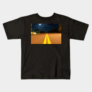 Yellow road lines stretch ahead in night light Kids T-Shirt